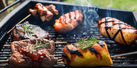 Assorted Meats And Vegetables Grilling On a Barbecue Grate Over Lump Charcoal.