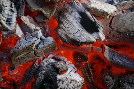 Glowing Red Charcoal Embers Under Ashy Logs Highlighting Lumpwood Charcoal’s Advantages.