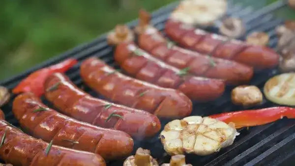 Barbecue grill plate with sausages and vegetables, black surface, metal construction.